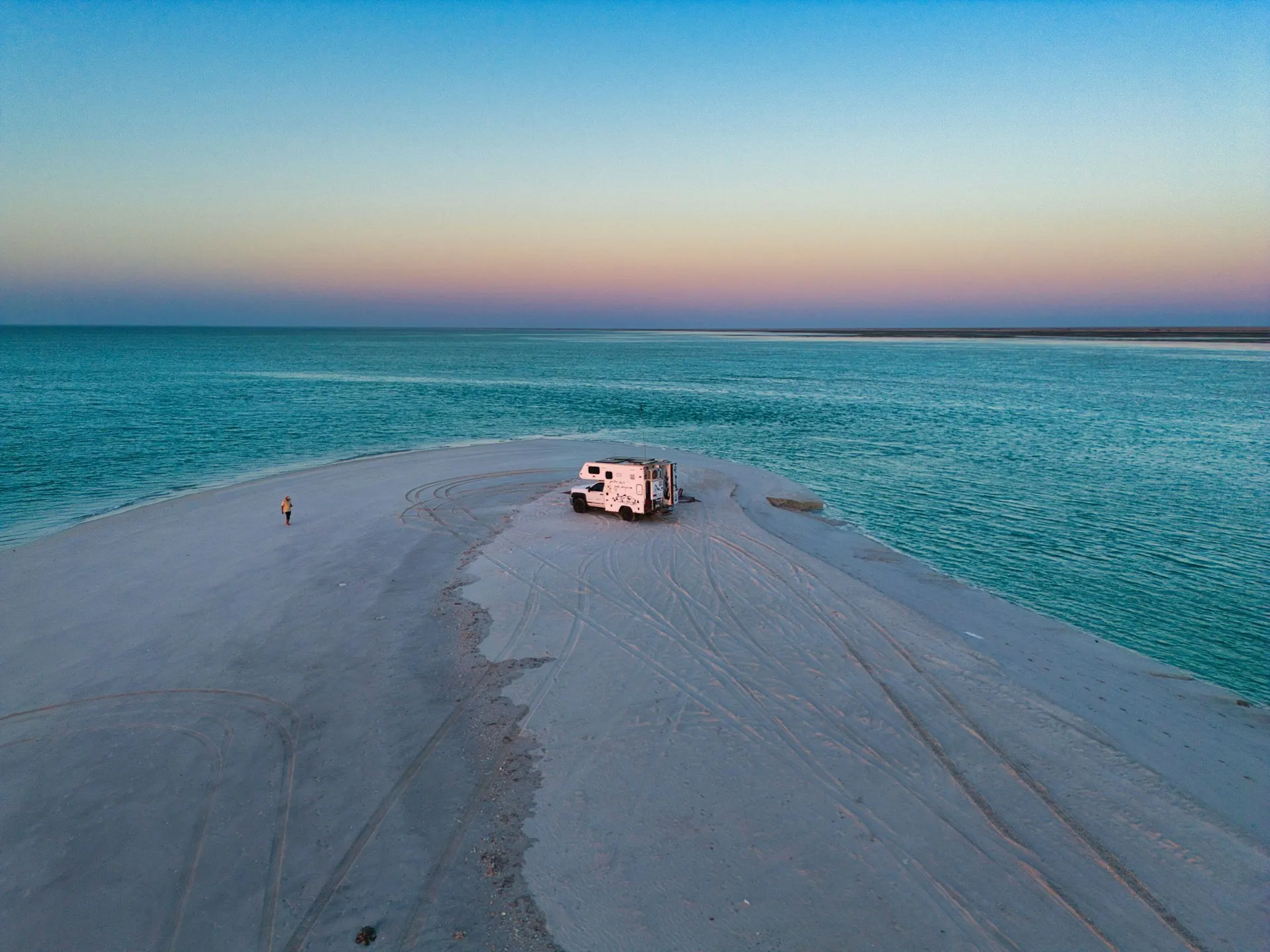 Campervan parked on sandy spit between turquoise ocean waters